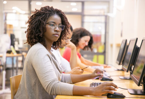 African American adult student working in computer class. Line of man and women in casual sitting at table, using desktops, typing. Staff training concept